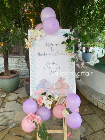 A charming welcome sign for a twins' baby shower, featuring sleeping bunnies and decorated with pastel balloons and flowers.