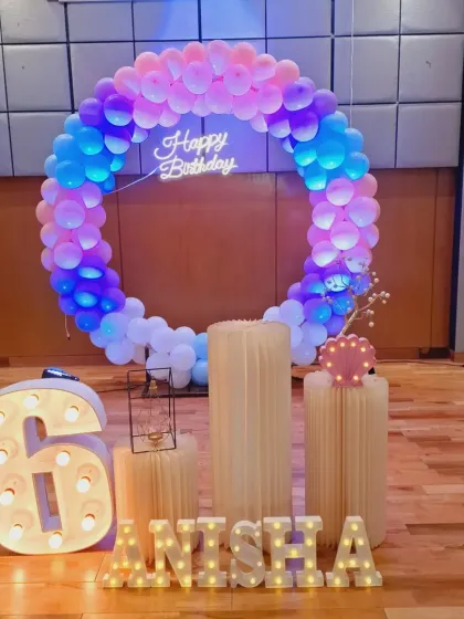 The lighting on this 6th birthday setup creates a beautiful glow, highlighting the pastel balloon colors and the neon "Happy Birthday" sign.