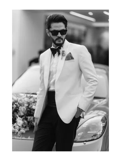 A dapper groom in a white tuxedo jacket, posing with a classic car. This black and white shot exudes cool confidence and timeless style.