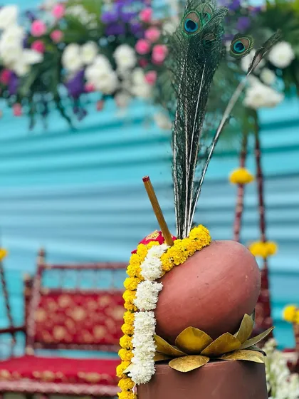 A detailed prop from a Krishna-themed event: a clay pot ('matki') decorated with a peacock feather and flower garland, symbolizing Lord Krishna.