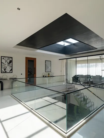 Natural light pours in from a large skylight over the central void, illuminating the upper floor and highlighting the clean, minimalist design with glass railings.