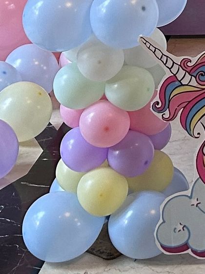A cluster of pastel-colored balloons at the base of a unicorn party setup. The soft blues, yellows, pinks, and purples create a dreamy, cloud-like effect.