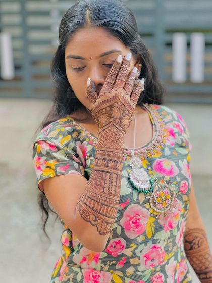 A shy pose from a client, her hand covering her face, drawing attention to the intricate henna work.