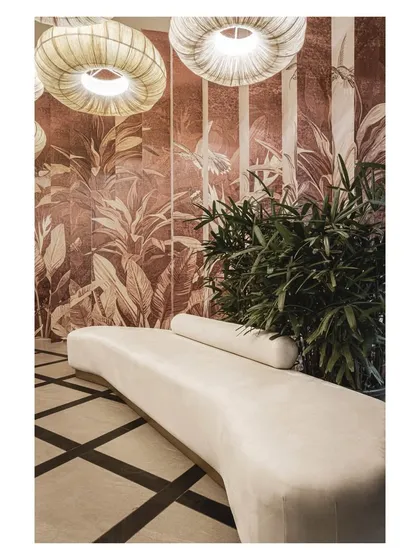 A custom curved bench in a soft, neutral fabric provides elegant waiting area seating. It sits against a backdrop of botanical wallpaper, introducing a touch of nature and softness to the lobby.