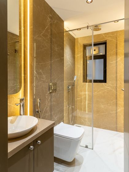 Wrapped in warm taupe and caramel-toned marble, this bathroom radiates understated luxury. The neutral palette is elevated by soft lighting and crisp white flooring, striking the perfect balance between elegance and calm.