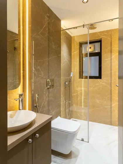 Wrapped in warm taupe and caramel-toned marble, this bathroom radiates understated luxury. The neutral palette is elevated by soft lighting and crisp white flooring, striking the perfect balance between elegance and calm.