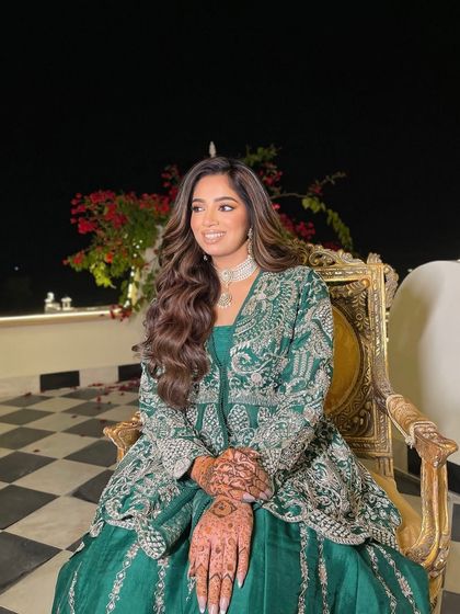 The bride seated in a beautiful setting. Her voluminous waves cascade over her shoulders, perfectly complementing her green and silver outfit.