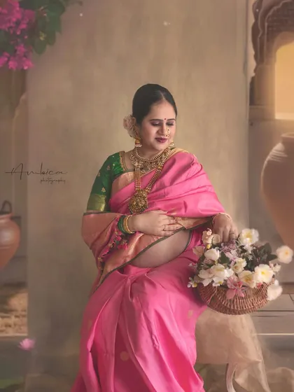 A wider shot from the same session, showing the mother-to-be with a basket of flowers. The custom-painted backdrop with architectural elements adds depth and context, creating a complete storytelling frame for this traditional maternity photoshoot.
