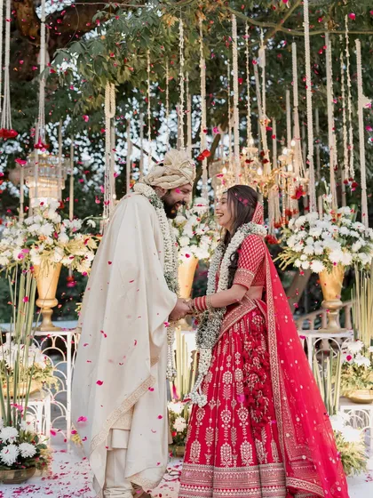 A classic sundowner wedding with a twist. The mandap is framed by an ancient tree, from which we hung floral strings and chandeliers, blending natural beauty with opulent design for a magical varmala moment.