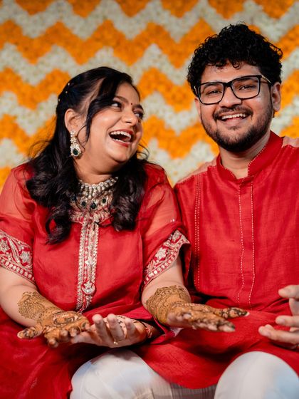 The couple sharing a laugh during their Mehendi, their coordinated red outfits perfect for the festive occasion.
