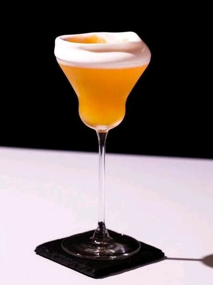 A sophisticated whiskey sour or similar frothy cocktail. Served in a unique, modern glass, this drink is perfect for a formal or upscale event.