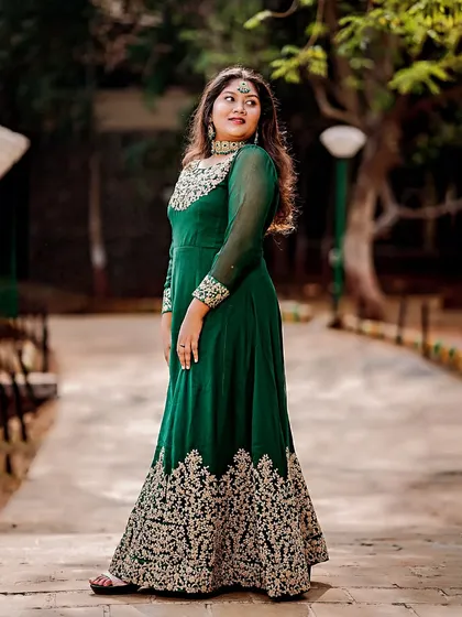 A classic portrait pose in a park setting, highlighting the rich color and detailed golden embroidery of the traditional gown.