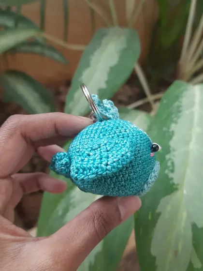 A side view of the little blue creature keychain. The shape is simple and round, making it a perfect handful of cute.