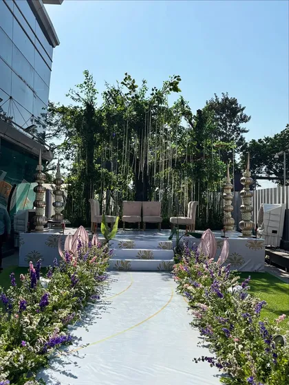 A wide shot of the royal aisle and stage, showing the full grandeur of the outdoor setup with its lush floral borders and elegant seating.