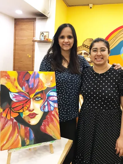 A student and I stand beside her vibrant, abstract portrait of a woman with butterfly wings, a powerful piece full of color and emotion.