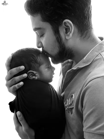 A father's gentle love. This intimate black and white photo captures a tender moment as a father kisses his newborn's forehead. These are the precious memories we aim to preserve.