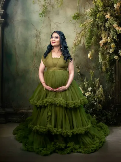 This is a more classic portrait using the same beautiful green gown. The pose highlights the baby bump against a painterly backdrop, creating a look of timeless grace.