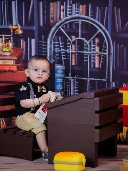 A studious-looking baby sitting at a miniature school desk in our library theme, perfect for capturing a quirky and fun personality.