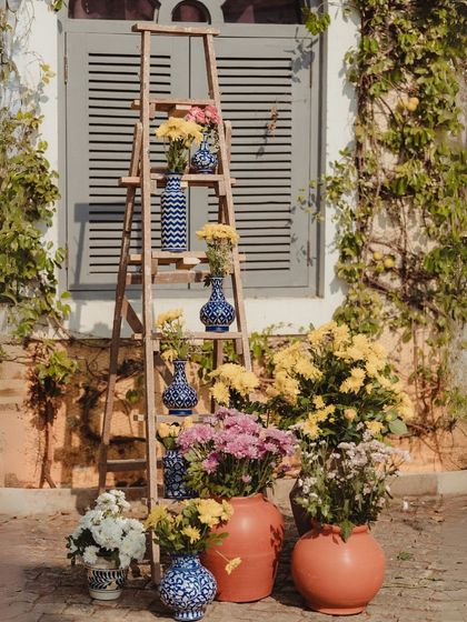 A beautiful decor detail using a rustic wooden ladder as a shelf to display an array of blue and white patterned vases with yellow flowers.