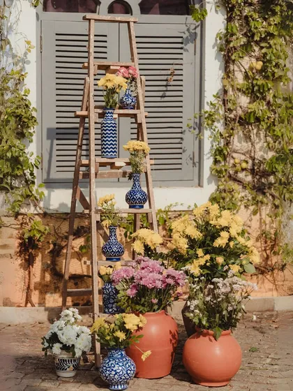 A beautiful decor detail using a rustic wooden ladder as a shelf to display an array of blue and white patterned vases with yellow flowers.