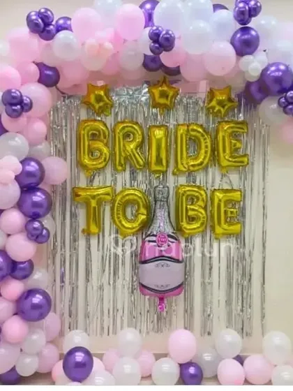 A 'Bride to be' home decoration with a purple, pink, and white balloon arch against a silver shimmer curtain.