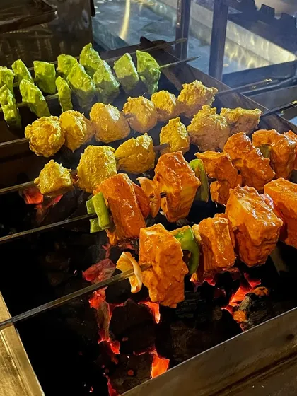 A variety of paneer and vegetable skewers grilling over hot coals. I offer different marinades, like a green herb one, a yellow one, and the classic red tandoori, to cater to different tastes.