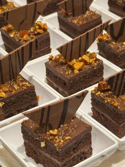 A tray of rich, multi-layered chocolate pastries. Each square is a decadent combination of cake, mousse, and crunchy nuts, perfect for a luxurious finish.