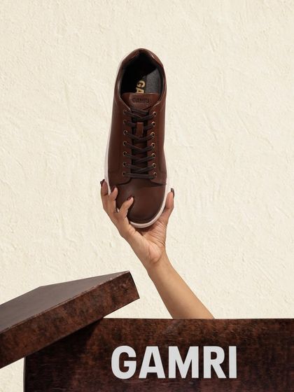 A hand holding a brown leather sneaker out of its box. This creative shot adds a human touch and a sense of discovery.