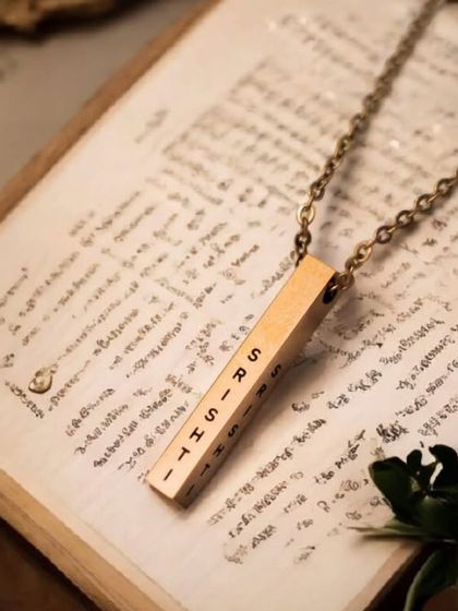 A rose gold bar pendant engraved with the name 'Sirisha', styled with a vintage book. This image evokes a sense of timelessness and storytelling.