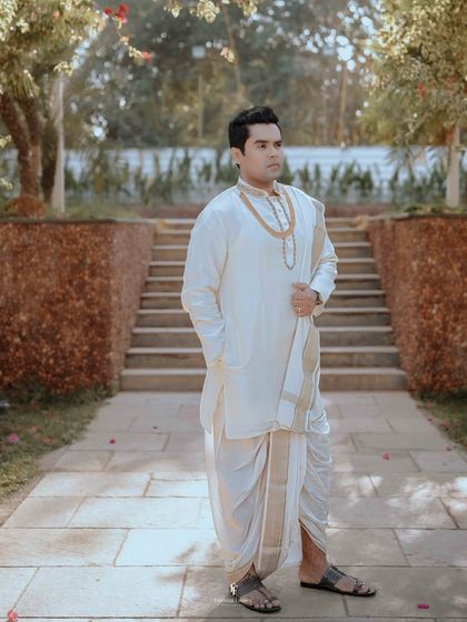 A full-length portrait of the groom in his traditional South Indian wedding attire.