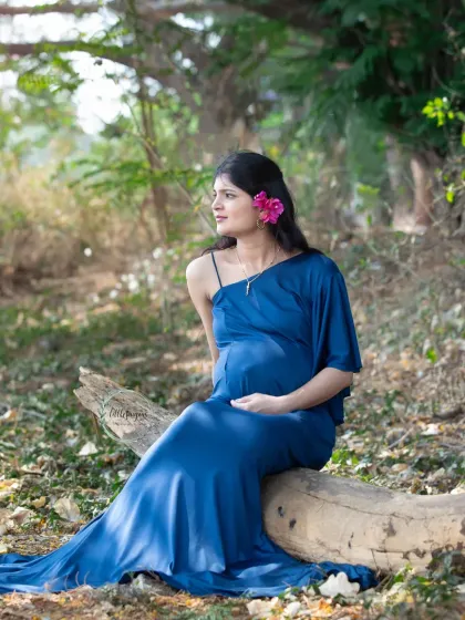 A dreamy, sun-kissed portrait in the forest. The mom-to-be sits peacefully on a log, her blue gown pooling around her, creating a magical and serene scene.