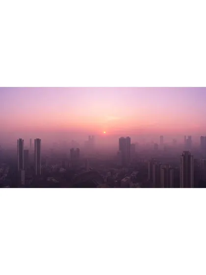 A wide, panoramic view of a hazy, purple sunset over the Mumbai skyline, creating a moody and atmospheric scene.