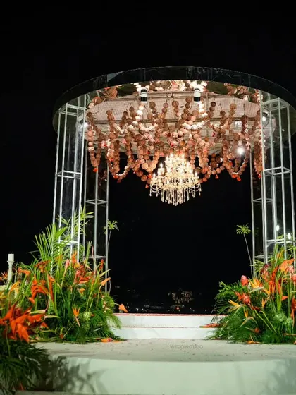 A modern mandap with a view. This structure, adorned with a floral and crystal chandelier and framed by tropical orange flowers, overlooks the water for a stunning ceremony backdrop.