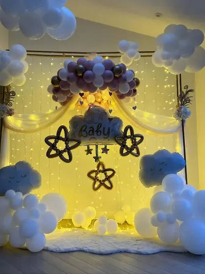 We brought a dreamy sky indoors for this baby shower. The setup features fluffy white balloon clouds, a warm backdrop of fairy lights, and a central balloon arrangement in pink and gold, creating a magical and serene atmosphere for welcoming the little one.