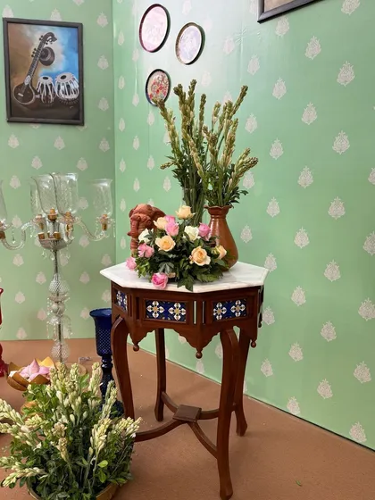 An antique-style side table with a floral arrangement, part of the detailed decor for the Ravi Varma-themed naming ceremony.