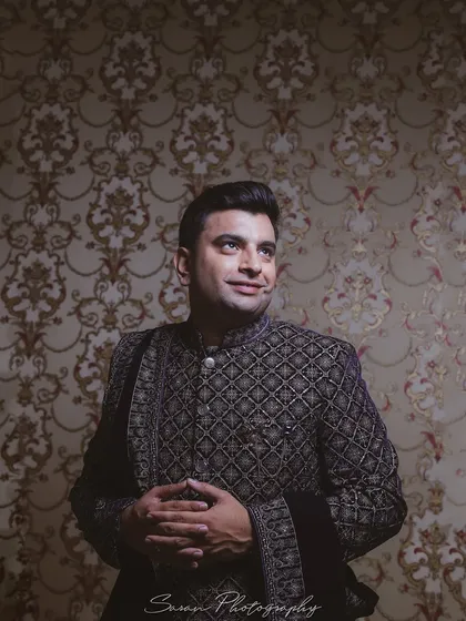 A handsome portrait of the groom in his intricately designed bandhgala, set against a classic patterned wallpaper.