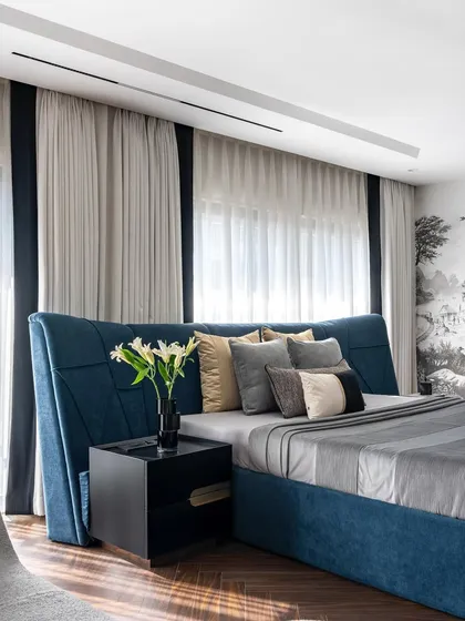 A close-up of the custom-designed bed in the Evelyn master bedroom. The deep blue fabric and unique winged headboard create a sense of drama and luxury, contrasting beautifully with the serene mural behind it.