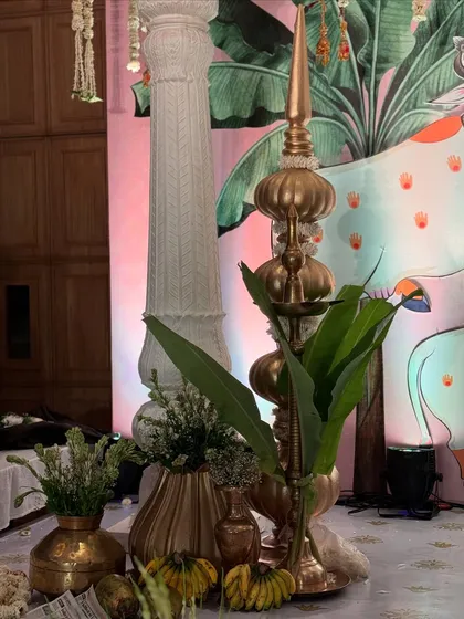A traditional golden finial (kalash) placed next to a white pillar, with a backdrop of Pichwai art, blending architectural and artistic elements.