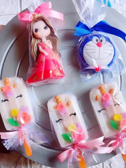 A collection of popular kids' soaps, including unicorn popsicles, a doll, and a Doraemon soap, all individually wrapped.