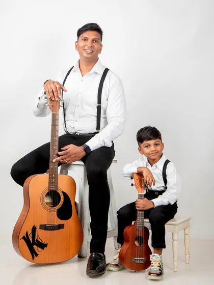 A "like father, like son" portrait, with both holding guitars and dressed in matching outfits.