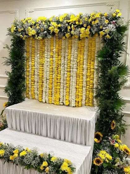 A bright and cheerful setup for any celebration, this backdrop uses strings of fresh yellow and white flowers, framed with dense greenery.
