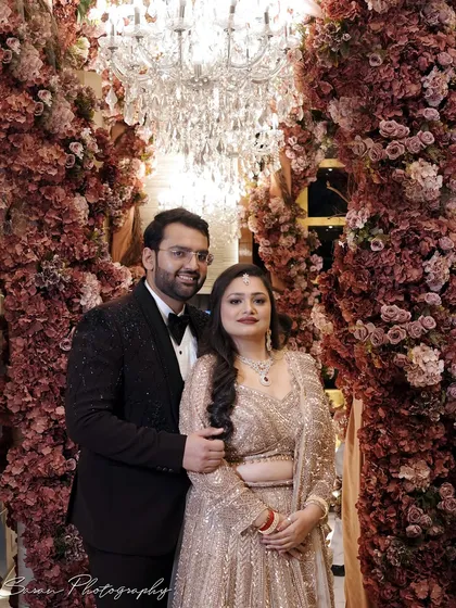 A classic couple portrait from an engagement, posing in front of a grand floral archway.