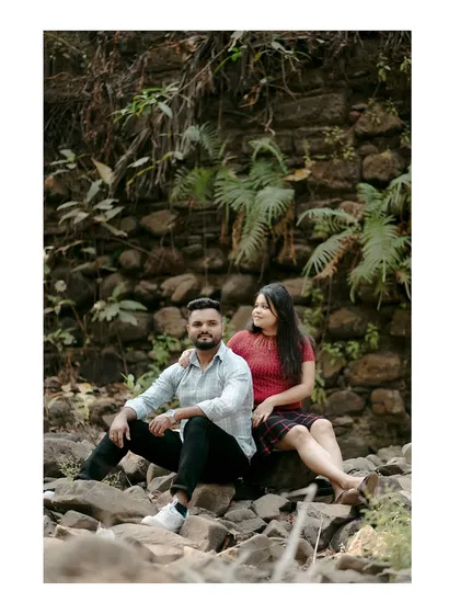 A casual, seated portrait against a rustic stone wall and greenery, showing the couple in a relaxed and natural state.
