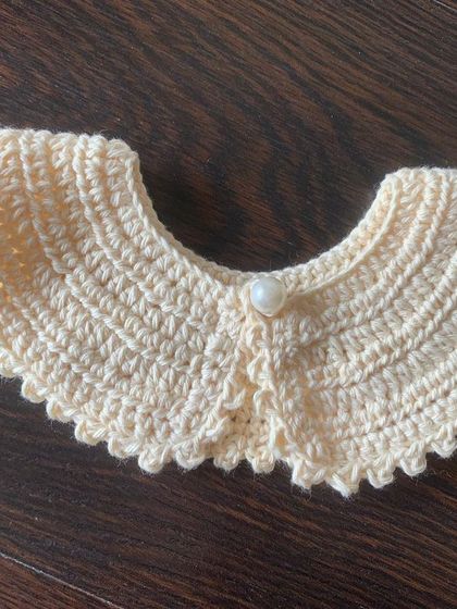 A close-up of the cream-colored detachable collar, highlighting the detailed stitch work and the central pearl button closure.