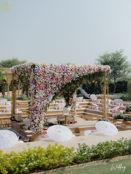 A wide view of the pastel floral mandap at Suryagarh, set within the venue's natural amphitheater. The addition of white parasols provided shade for guests and added a touch of whimsical charm to the elegant and romantic setting.