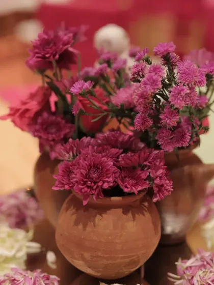 A centerpiece detail, with fresh purple flowers arranged in small, rustic terracotta matkas.