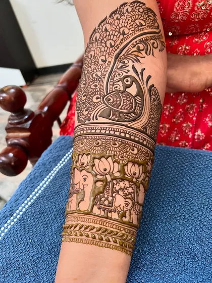 A close-up of a bridal arm piece, featuring a large peacock surrounded by lotus and elephant motifs.