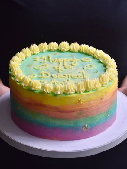 A vibrant rainbow birthday cake with a watercolour buttercream effect and delicate gold leaf flecks. This cheerful and colourful cake is a popular choice for bringing a splash of joy to any birthday party.