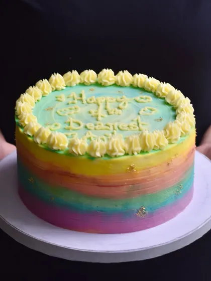A vibrant rainbow birthday cake with a watercolour buttercream effect and delicate gold leaf flecks. This cheerful and colourful cake is a popular choice for bringing a splash of joy to any birthday party.