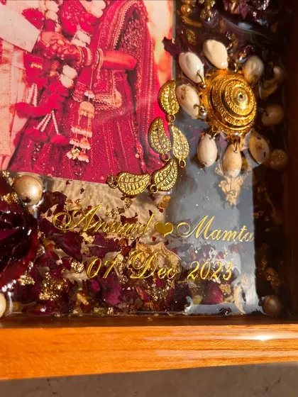 A close-up of a teakwood frame showcasing preserved kaleera and varmala flowers. The intricate details of the ornaments and the texture of the petals are captured perfectly in the resin.